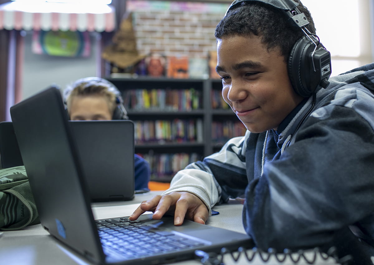 A young student smiles while taking an assessment on a laptop.